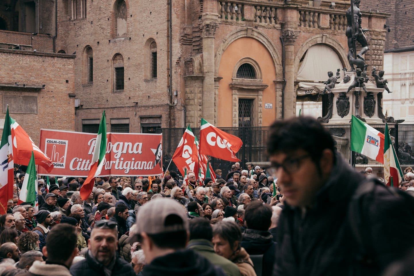 Manifestanti con bandiere italiane e sindacali si radunano in una piazza cittadina.